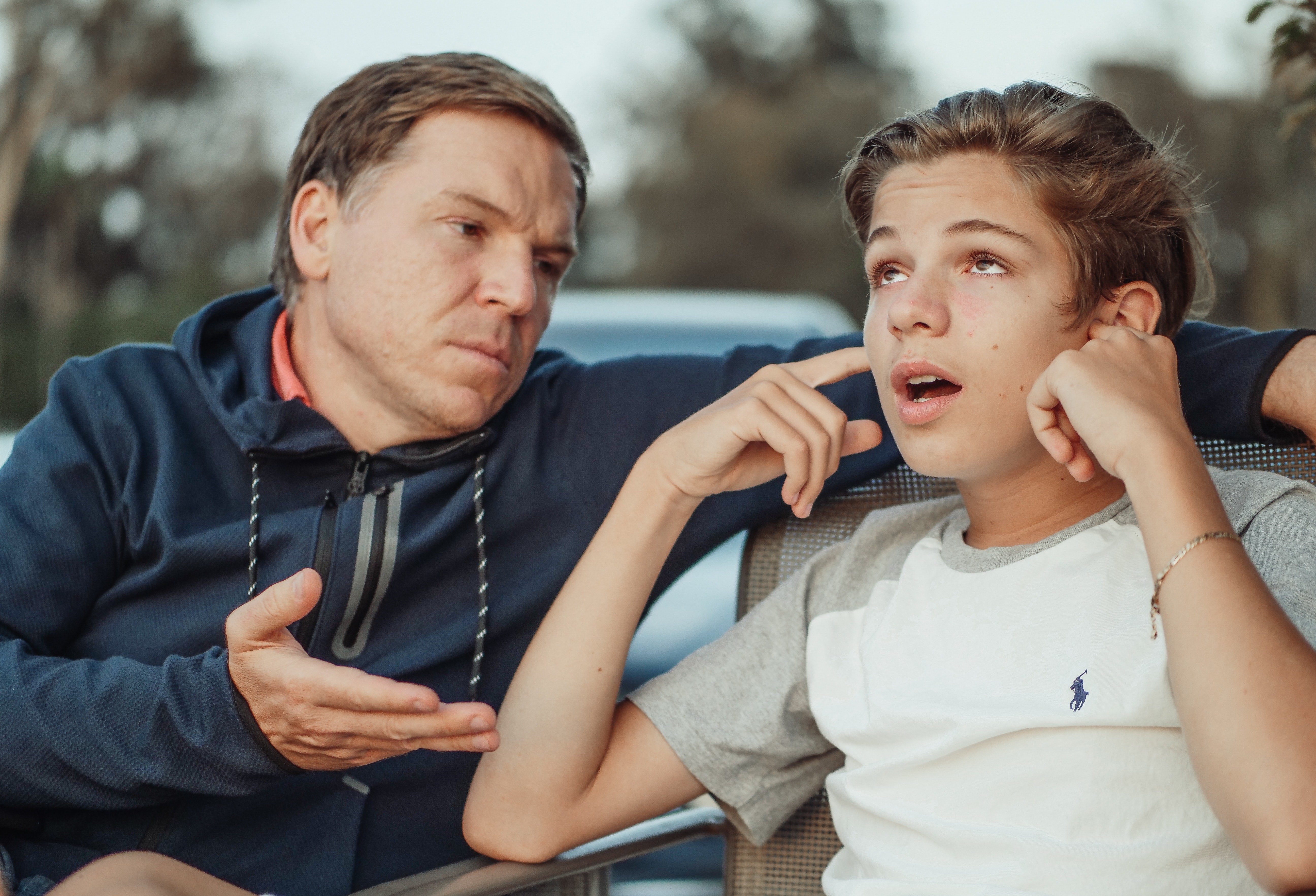 image of a father talking to son who has fingers in his ears