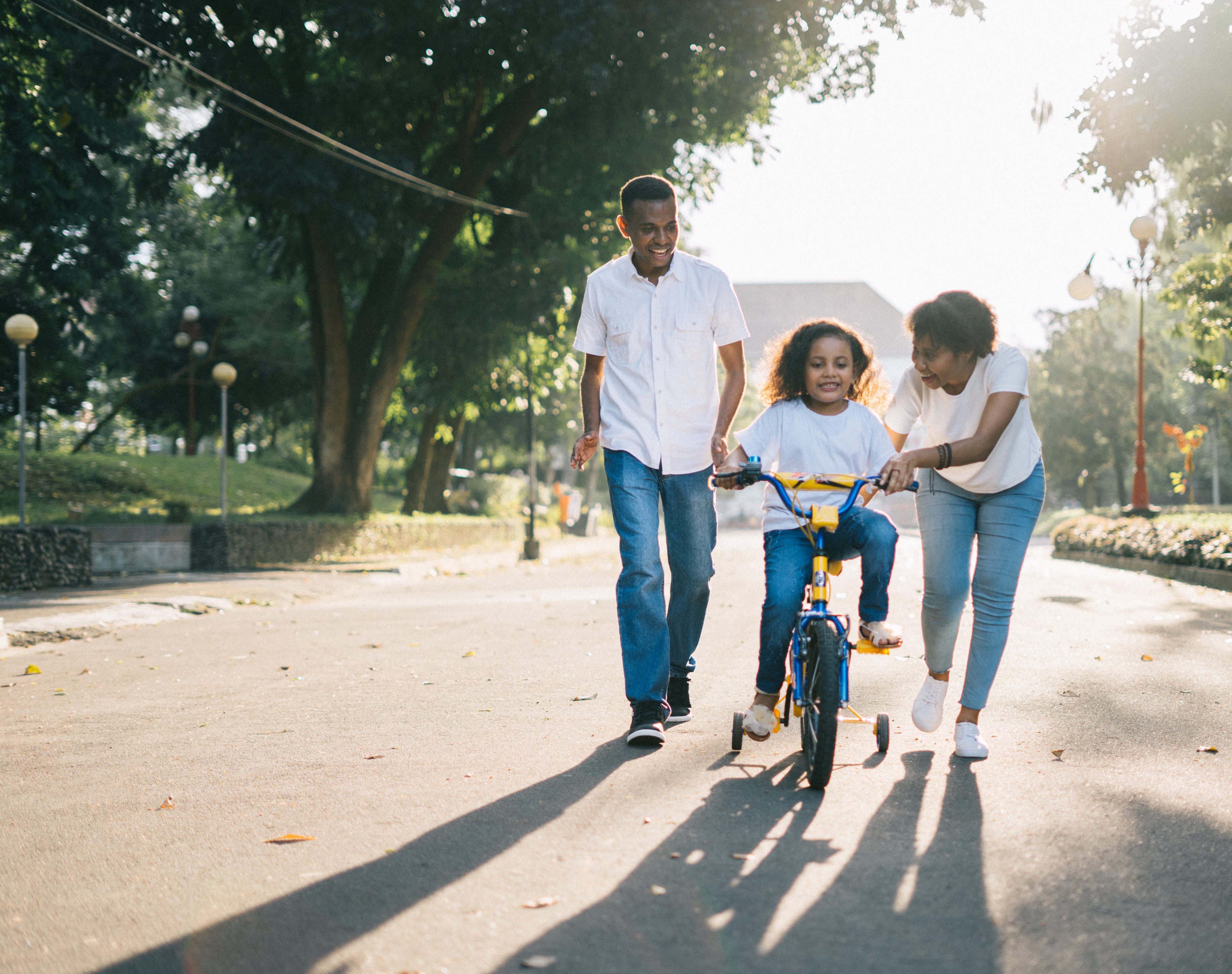 image of mom and dad helping daughter learn to ride bike