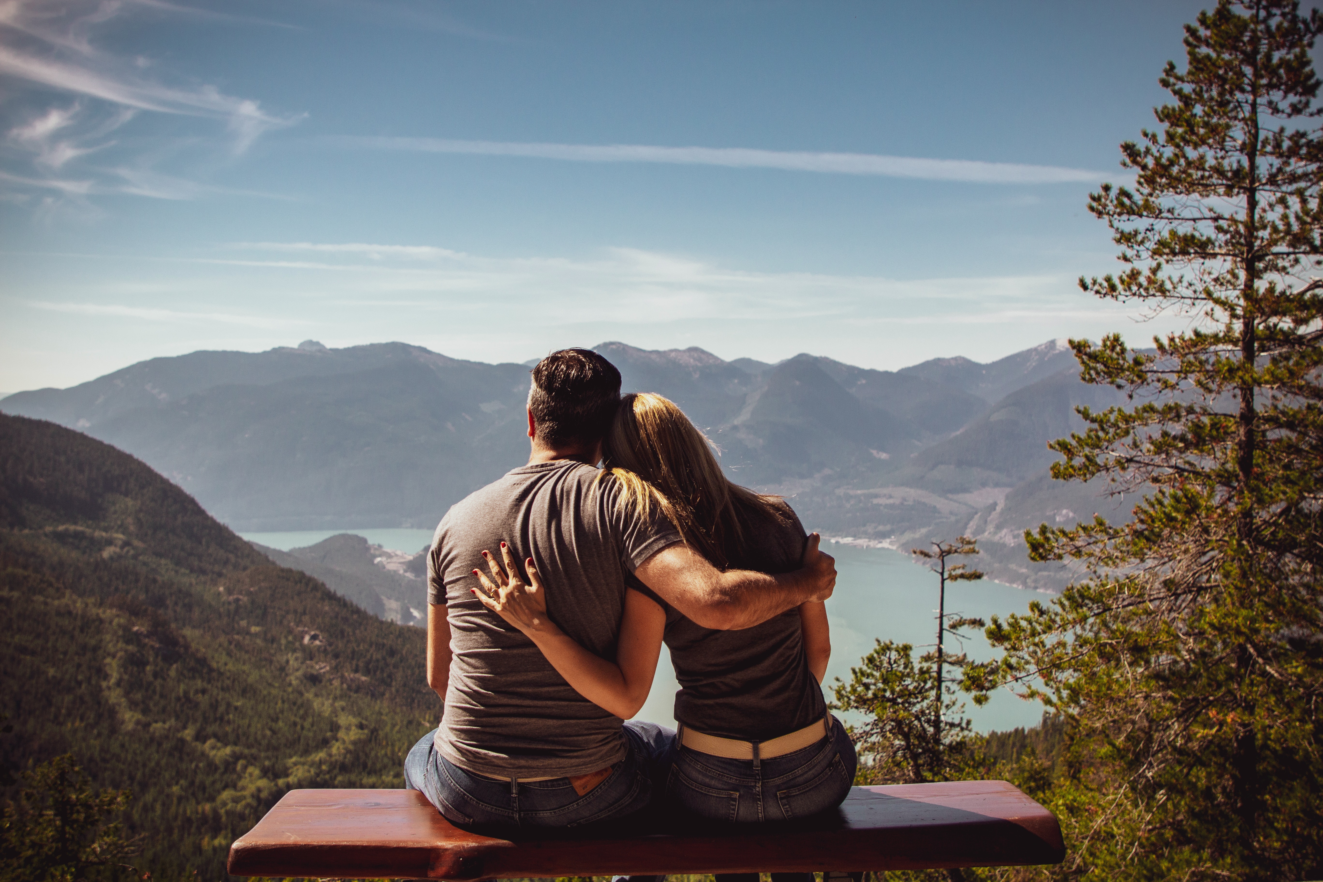 Man and woman sitting facing mountain with arms around each other
