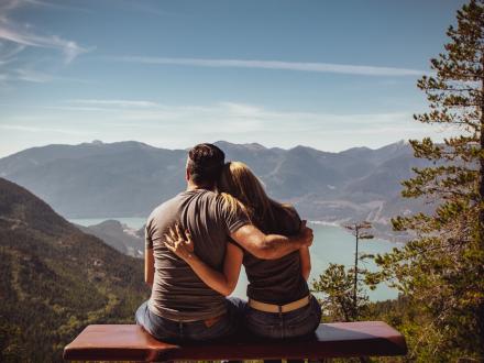 Couple sitting facing mountain with their arms around each other